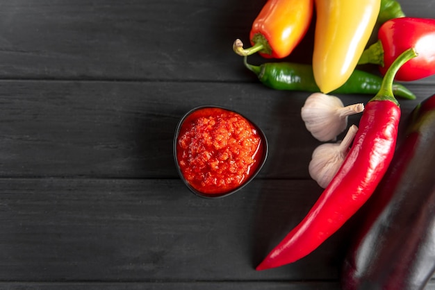 Ajvar in a black bowl with the ingredients red pepper chili peppers garlic on a wooden background a