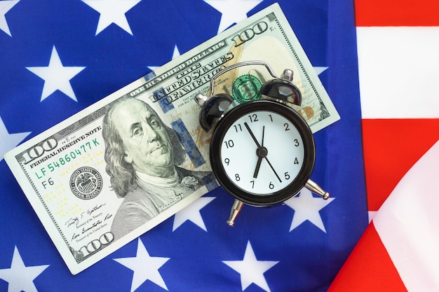 Alarm clock and 100 dollar banknote on American flag