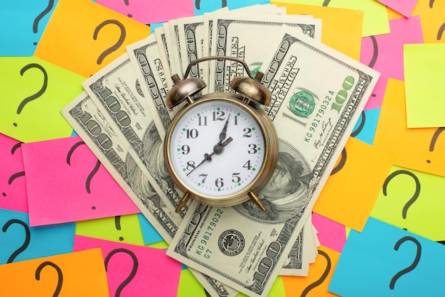 Photo alarm clock on the background of question marks and us dollars the concept of earning money ideas for salary and loss of time and money