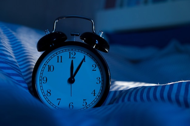 Alarm clock on bed in dark bedroom at night time.