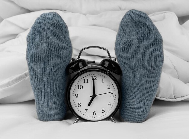 Alarm clock on bed next to female feet in socks