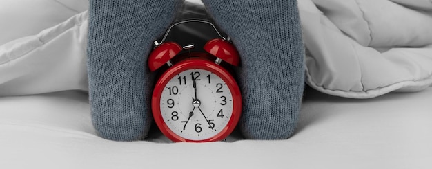 Alarm clock on bed next to female feet in socks