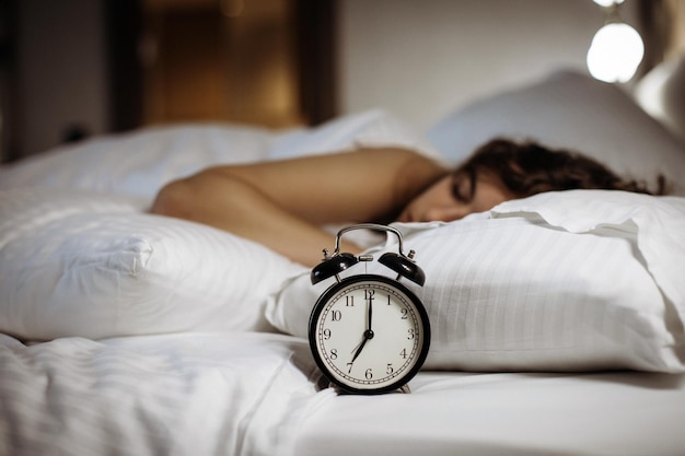 Alarm clock on the bed with sleeping woman behind