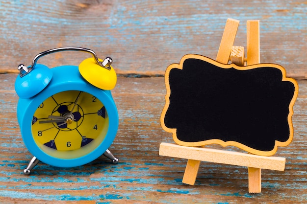 Alarm clock and a blackboard with empty space for a text on wooden background.