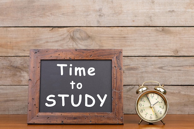 Alarm clock and blackboard with text Time to study on brown wooden background