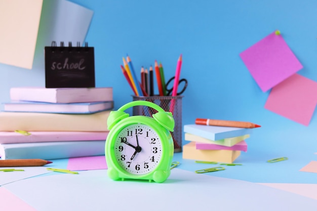 Alarm clock, books and stationery on pastel colors background of colorful paper, back to school