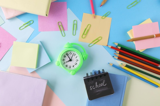 Alarm clock, books and stationery on pastel colors background of colorful paper, back to school