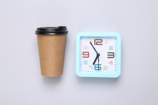 Alarm clock and craft coffee cup on gray background