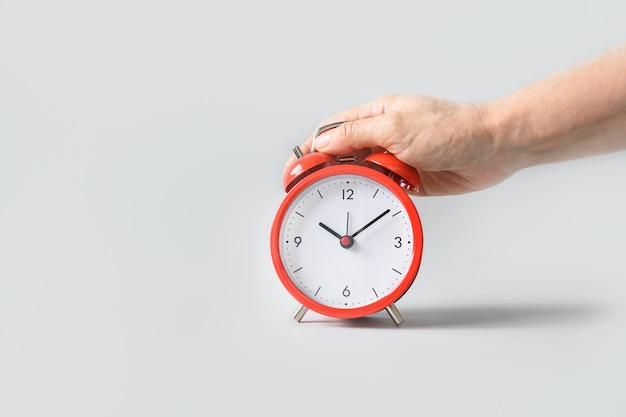 Alarm clock in female hand on gray background