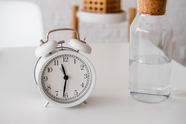 alarm clock and glass bottle with water on the table. Time to drink some water. Daily habits. Good habits.