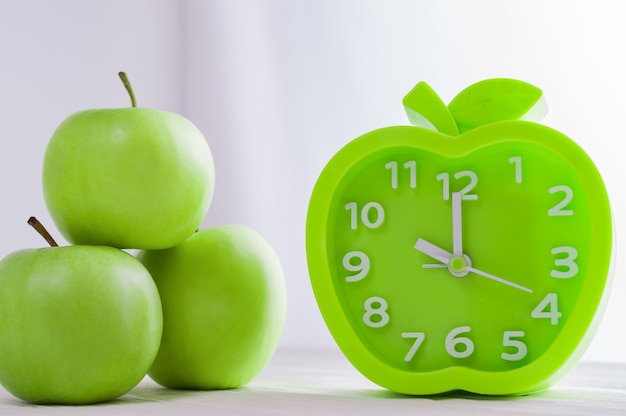 Alarm clock and green apples on white wooden table