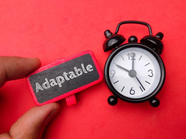 Alarm clock and hand holding wooden board with word Adaptable