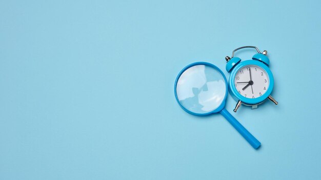 Alarm clock and magnifying glass on a blue background symbolizing the concept of a deadline