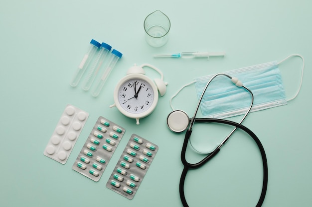 Alarm clock and medical tools on blue background, top view. Healthcare and early diagnostic concept