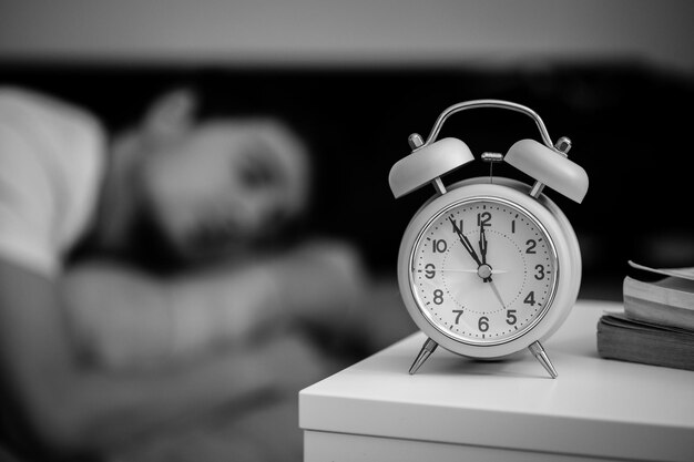 Alarm clock in the morning Young man sleeps in the blurry background