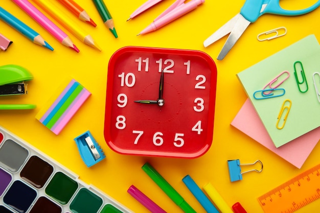 Alarm clock paint pencils and scissors School accessories on a yellow background Back to school concept