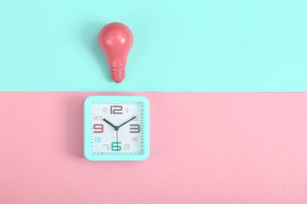 Alarm clock and pink light bulb on pink blue background Minimalism Top view