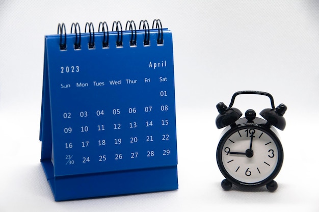 Alarm clock pointing at 9 o39clock with April 2023 calendar on white background Time and calendar concept and copy space