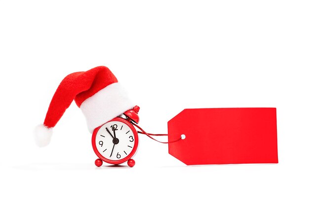 Alarm clock in santa claus hat with a blank sign for the inscription in red