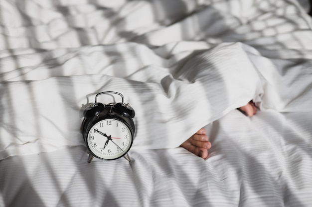 Alarm clock showing 7 oclock on the bed with sleeping person feet on blanket in the morning