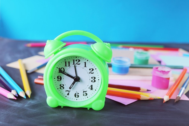 Alarm clock on the table, against the background of multi-colored paper, books and stationery