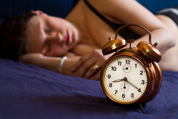 Alarm clock on table and woman sleeping 