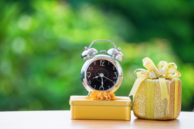 Alarm clock with gift box on green burred background.