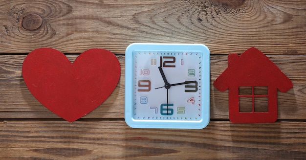 Alarm clock with red heart and house on wooden background Top view