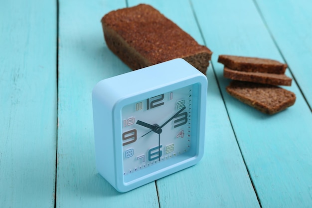 Alarm clock with Sliced whole grain rye bread on blue wooden background