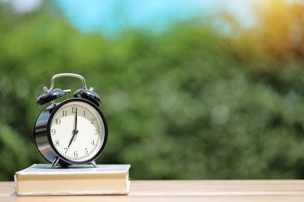 Alarm clock with white book on wooden desk 