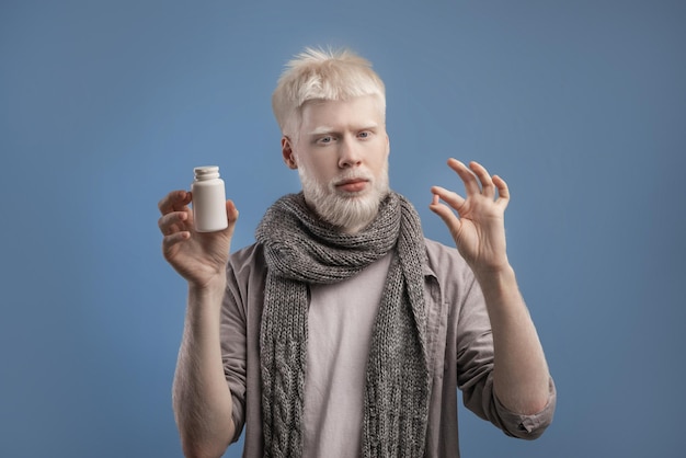 Albino guy holding jar with meds and pill in hands standing on blue background taking anti viral