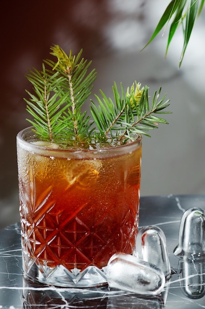 Alchohol cocktail on old-fashioned glass decorated pine branches with cones closeup. cocktail on marble table, bar concept