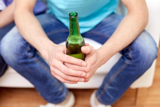 Photo alcohol and people concept - men with beer bottles sitting on sofa at home