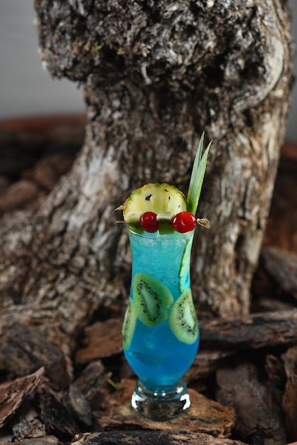 Alcoholic cocktail Blue Lagoon with ice, a piece of pineapple and kiwi on a background of tree bark