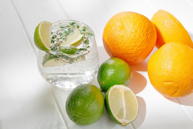 Alcoholic cocktail in a glass on a light background with lime and thyme and orange