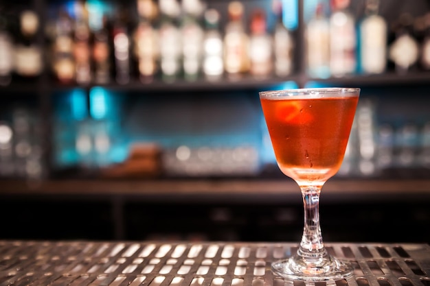 An alcoholic cocktail of red color with a decoration of lemon peel stands on a bar counter Horizontal photo