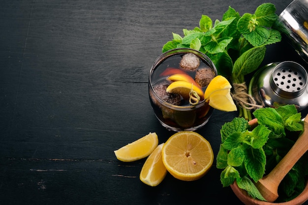 Alcoholic cocktail of whiskey lemon and mint RumCola Brandy On a black wooden background Free space for text