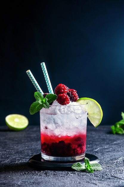 Alcoholic Cocktail with Rum or  Soda, Raspberry and Blackberry Puree, Lime and Mint in the Glass on the Dark Grey wall