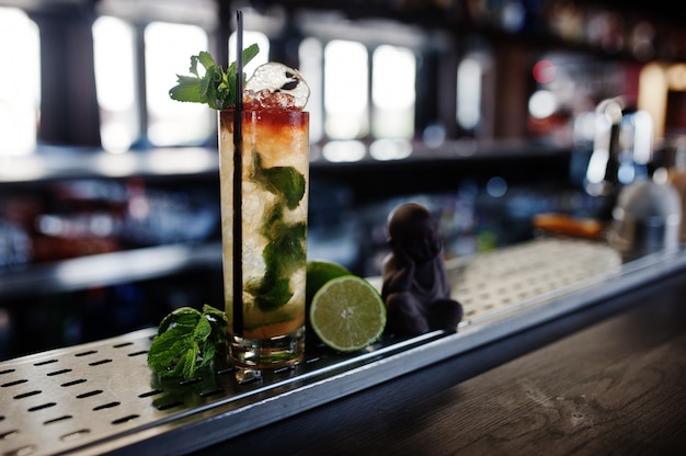 Alcoholic long cocktail with mint and lime in glass at bar table