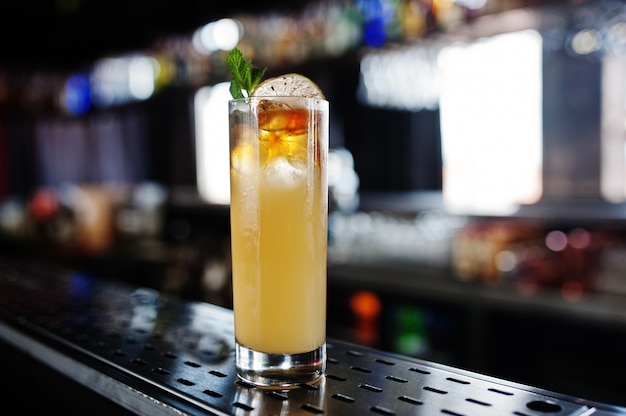 Alcoholic long yellow cocktail in glass at bar table