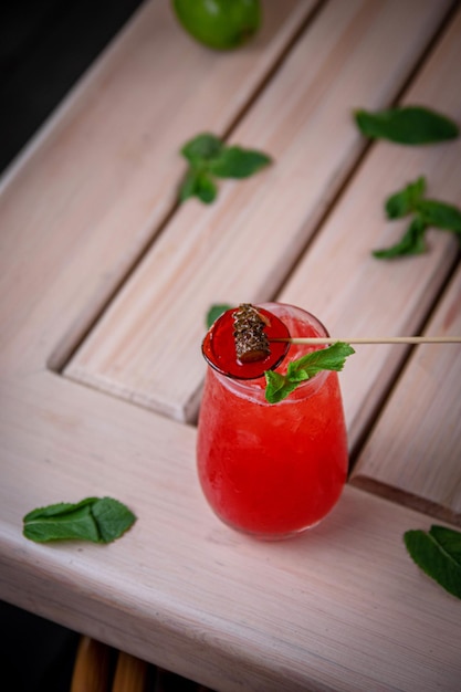 Alcoholic refreshing gin tonic cocktail with strawberry juice lollipop and mint with ice cubes on the summer terrace of the restaurant