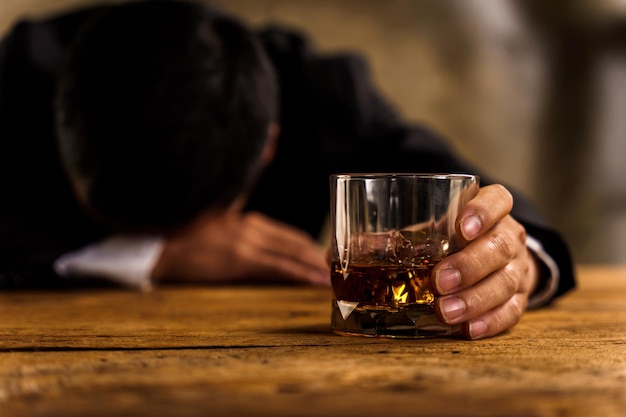 Alcoholism depressed asian young man sleep on table while drinking alcoholic beverage holding glass of whiskey alone at night Treatment of alcohol addiction suffer abuse problem alcoholism concept