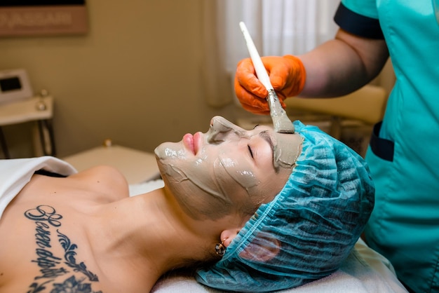 Alginate face mask application process A female hands of a beautician holding spatula Woman lying on a couch in office of cosmetologist Facial skincare in the beauty spa salon