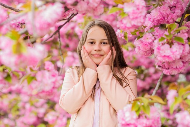 Allergy remedy Child enjoy life without allergy Sniffing flowers Girl enjoying floral aroma Pollen allergy concept Kid enjoy cherry blossom sakura Kid on pink flowers sakura tree background