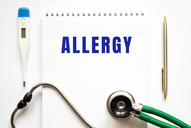 ALLERGY text written in a notebook lying on a desk and a stethoscope