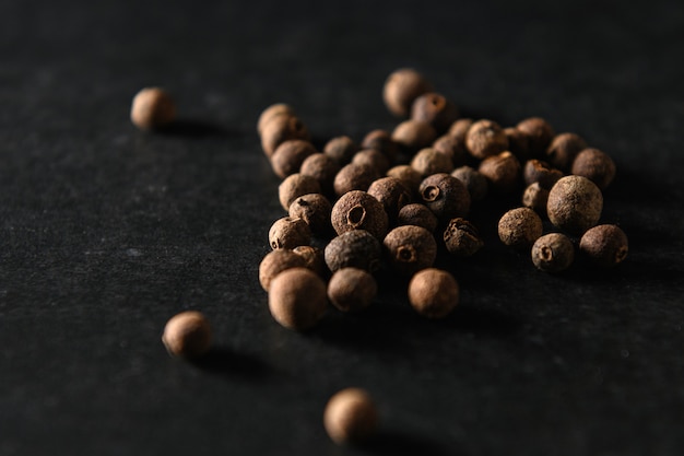 Allspice black peppercorns, seasoning for food, sprinkled on gray background