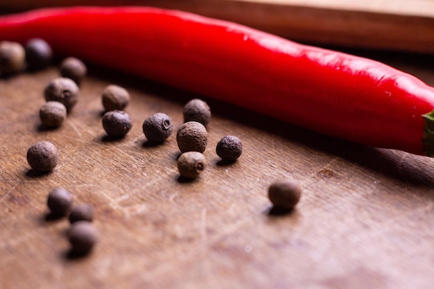 Allspice peas lies next to red capsicum on a wooden table