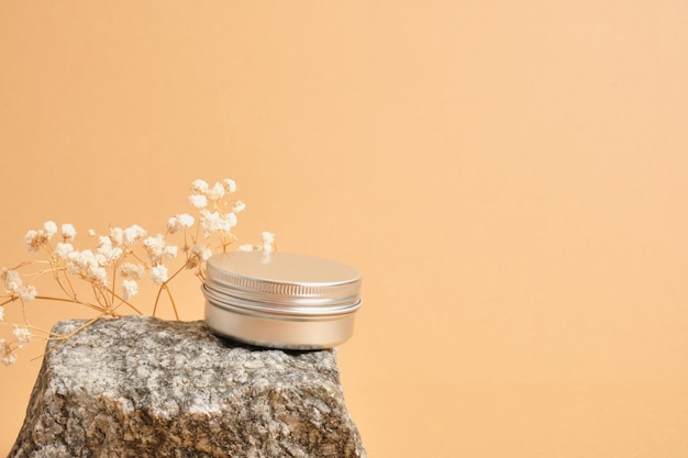 Alluminum cream jar on stone with dry flowers on beige background