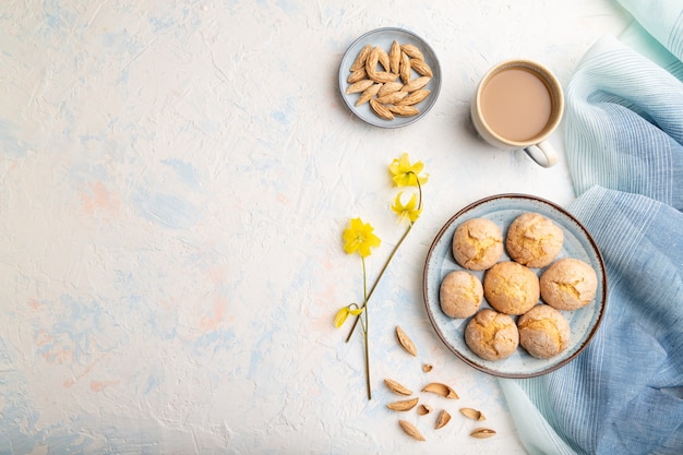 Almond cookies and a cup of coffee on a white concrete surface and blue linen textile