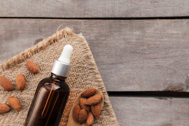 Almond essential oil in glass bottle with spoon. Cosmetic concept on wooden background with sackcloth, isolated flat lay.